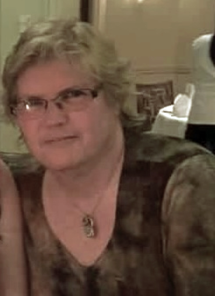 Brenda Shisslak, co-leader of the EDS and CTD New England/MA Support Group sits relaxed in a dining hall. A caucasian woman with glasses and short, wavy blonde hair, she wears a beautiful gemstone necklace.