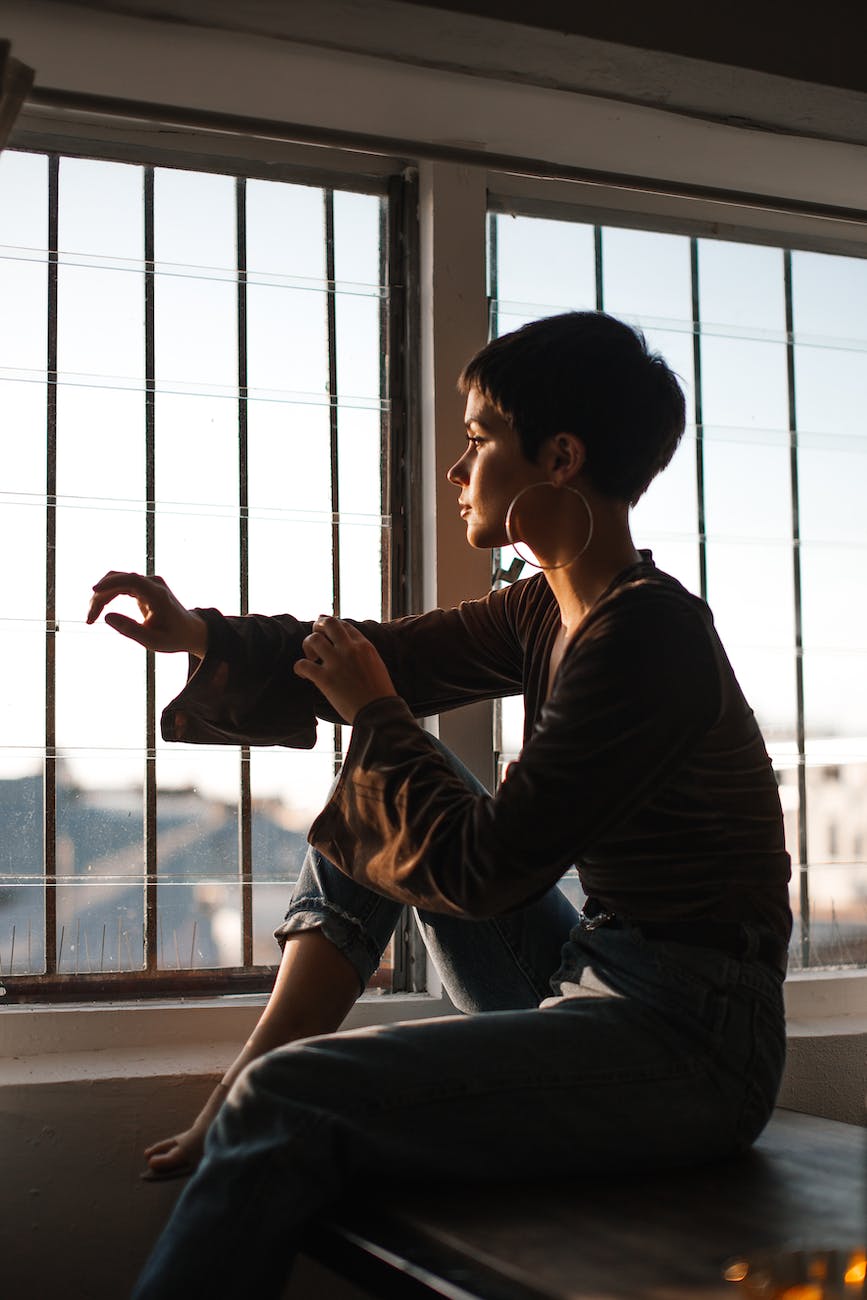 A young woman sits before a barred window in silhouette, with a bright blue sky beyond.